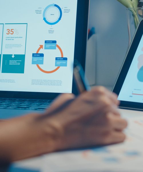 Close-up young asia lady freelance focus on laptop write workshe Close-up young asia lady freelance focus on laptop write worksheet finance graph account chart market plan in laptop and tablet at house. Girl student learn online, Work from home night concept.