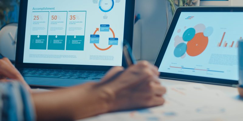 Close-up young asia lady freelance focus on laptop write worksheet finance graph account chart market plan in laptop and tablet at house. Girl student learn online, Work from home night concept.