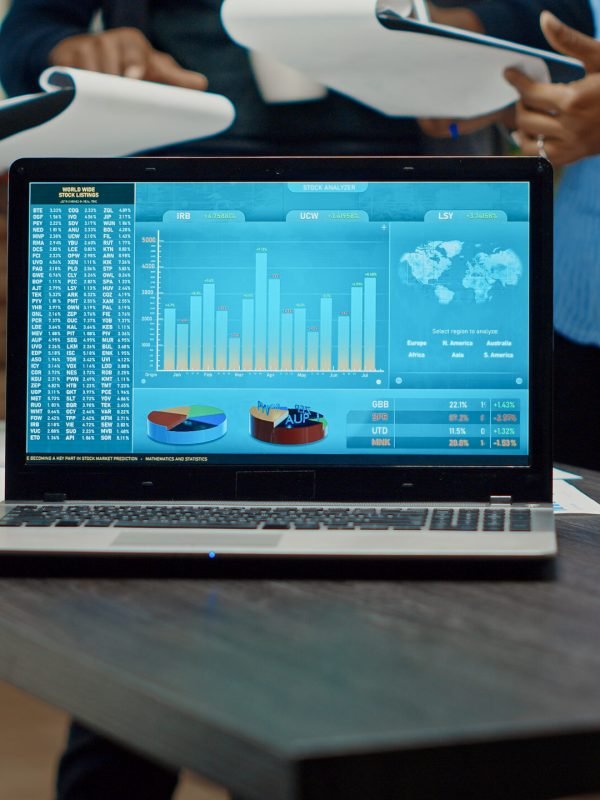 Laptop running online analytics data in boardroom meeting, business people discussing new development strategy. Annual reports with official corporate information, statistics.